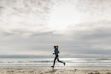 Spain, Tarragona, Woman running on a beach in winter - JRFF000339