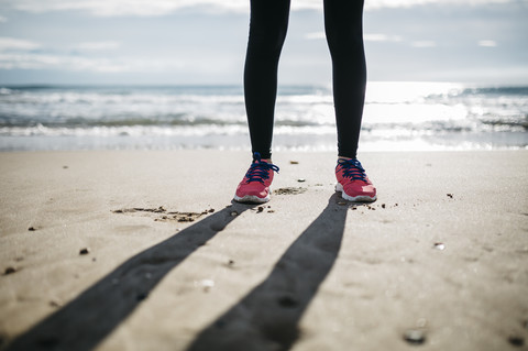 Beine und Turnschuhe auf dem Sand eines Strandes, lizenzfreies Stockfoto