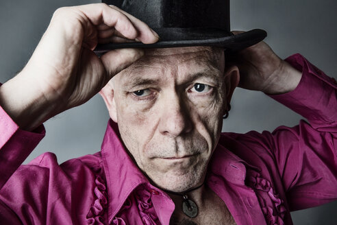 Portrait of man wearing pink shirt with frills putting on top hat - JATF000819