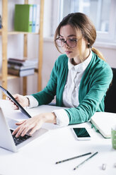 Junge Geschäftsfrau arbeitet mit Laptop und digitalem Tablet im Büro - AKNF000033