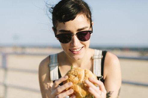 USA, New York, Coney Island, young woman eating a hamburger - GIOF000625