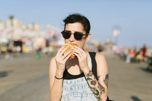 USA, New York, Coney Island, young woman eating a hamburger - GIOF000626