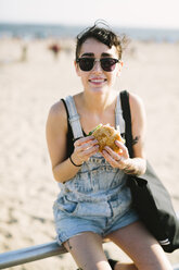 USA, New York, Coney Island, junge Frau isst einen Hamburger am Strand - GIOF000628