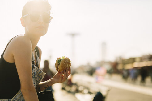 USA, New York, Coney Island, young woman eating a hamburger - GIOF000629