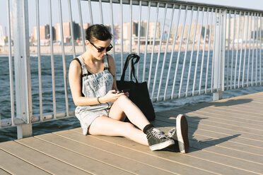 USA, New York, Coney Island, junge Frau, die auf dem Pier ihr Telefon überprüft - GIOF000635