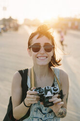 USA, New York, Coney Island, lächelnde junge Frau, die bei Sonnenuntergang fotografiert - GIOF000663