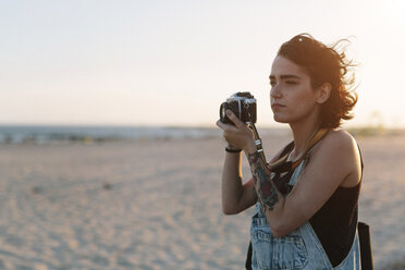 USA, New York, Coney Island, young woman taking photos on the beach at sunset - GIOF000671