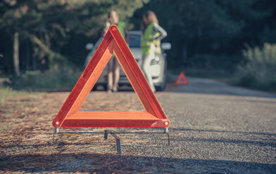 Warndreieck auf der Straße bei einer Autopanne mit Frauen im Hintergrund - DAPF000012