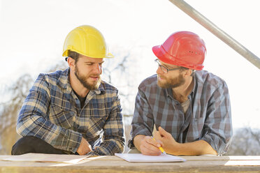 Two craftsmen discussing and taking notes in construction site - LAF001594