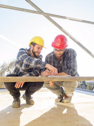 Two craftsmen discussing and taking notes in construction site - LAF001595