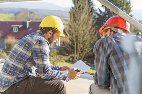 Zwei Handwerker schauen sich auf einer Baustelle Notizen an, lizenzfreies Stockfoto