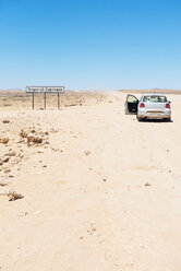 Namibia, Namib-Wüste, Swakopmund, leeres Auto mit offener Tür auf einer staubigen Piste neben dem Wendekreis-Schild - GEMF000644
