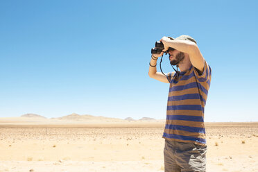 Namibia, Namib-Wüste, Mann mit Hut benutzt ein Fernglas, um wegzuschauen - GEMF000645