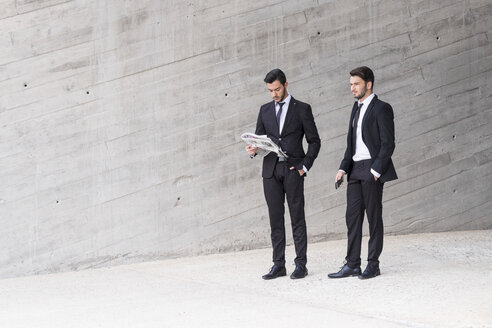Zwei Geschäftsleute in schwarzen Anzügen stehen vor einer Betonwand - SIPF000071