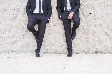 Zwei Geschäftsleute in schwarzen Anzügen lehnen Seite an Seite an der Wand - SIPF000075