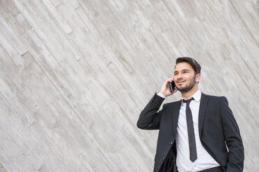 Portrait of smiling businessman wearing black suit telephoning with smartphone - SIPF000088