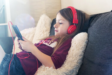 Mädchen sitzt auf der Couch und hört Musik mit Kopfhörern und digitalem Tablet - SARF002461