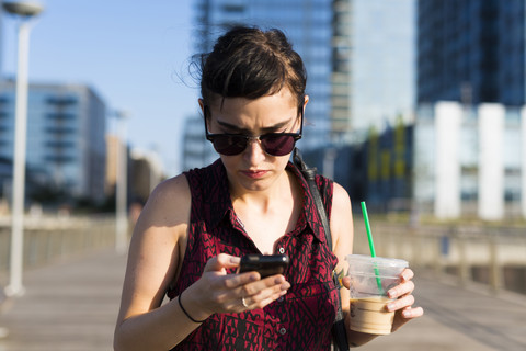 Porträt einer jungen Frau, die auf ihr Smartphone schaut, lizenzfreies Stockfoto