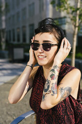 Portrait of tattooed young woman with headphones and sunglasses - GIOF000705