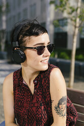 Portrait of tattooed young woman with headphones and sunglasses - GIOF000706