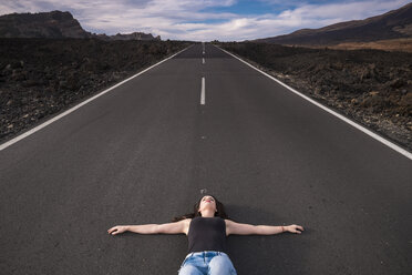 Spain, Tenerife, woman lying on an empty road with outstretched arms - SIPF000114