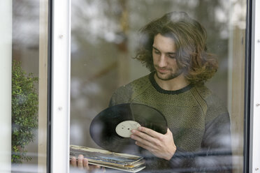 Junger Mann mit Schallplatten hinter Fensterscheibe stehend - LBF001351