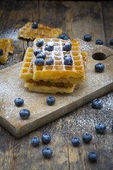 Stack of waffles with icing sugar and blueberries on wooden board - LVF004448
