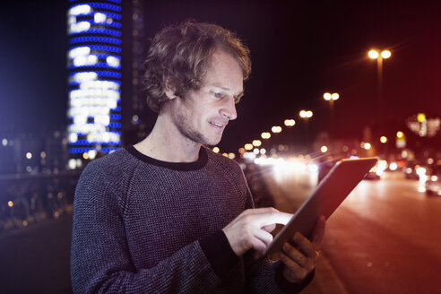Deutschland, München, Porträt eines Mannes, der bei Nacht ein digitales Tablet benutzt - RBF004070