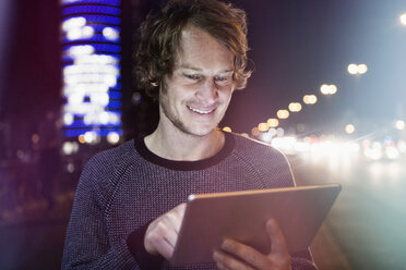 Germany, Munich, portrait of smiling man using digital tablet at night - RBF004071