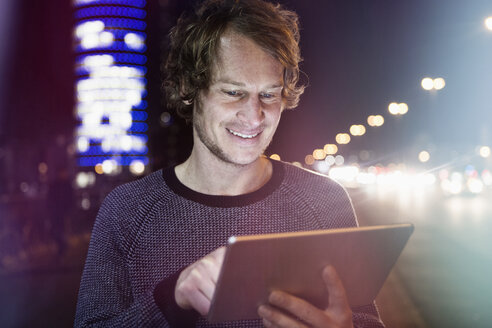 Deutschland, München, Porträt eines lächelnden Mannes, der ein digitales Tablet bei Nacht benutzt - RBF004071