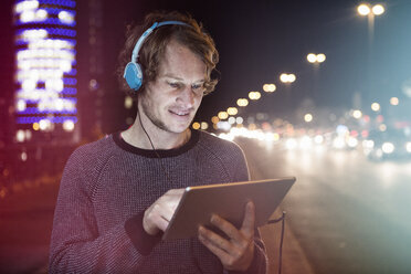 Germany, Munich, portrait of man with headphones using digital tablet at night - RBF004072