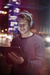 Germany, Munich, man with headphones using digital tablet at night - RBF004077