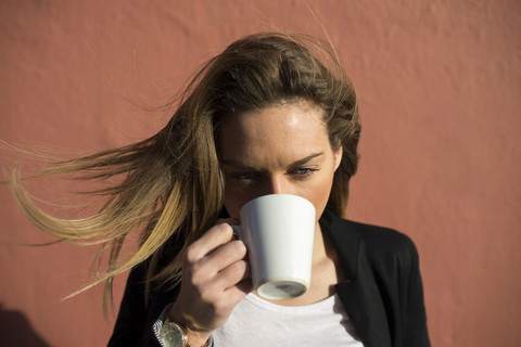 Frau mit wehendem Haar trinkt Kaffee, lizenzfreies Stockfoto