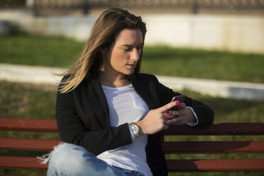 Frau sitzt auf einer Bank und schaut auf ihr Smartphone - KIJF000125
