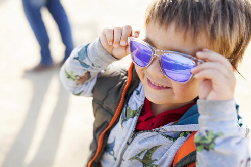 Porträt eines lächelnden kleinen Jungen, der eine bunte Sonnenbrille aufsetzt - VABF000073