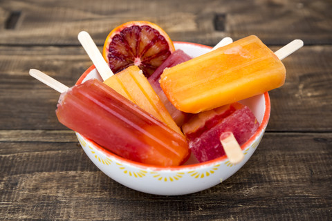 Bowl of different homemade orange ice lollies and blood orange slice stock photo