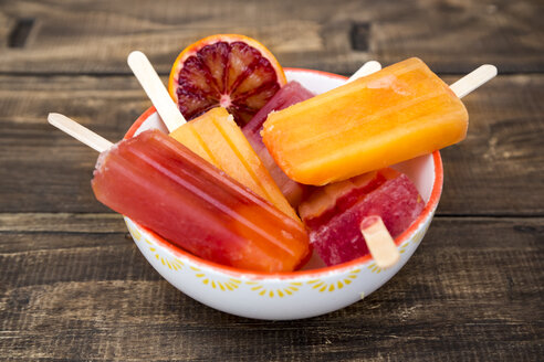 Bowl of different homemade orange ice lollies and blood orange slice - SARF002480