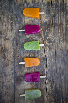 Row of fruit smoothie ice lollies on dark wood - LVF004455