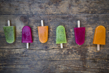 Row of fruit smoothie ice lollies on dark wood - LVF004456