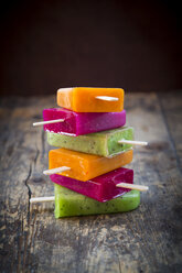 Stack of fruit smoothie ice lollies on dark wood - LVF004457