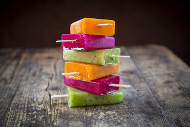 Stack of fruit smoothie ice lollies on dark wood - LVF004458