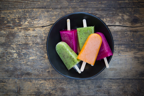 Bowl of fruit smoothie ice lollies on dark wood - LVF004459