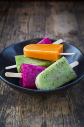 Bowl of fruit smoothie ice lollies on dark wood - LVF004460