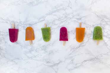 Row of fruit smoothie ice lollies on white marble - LVF004461