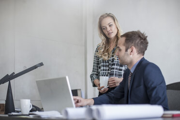 Businessman at desk with colleague looking at laptop - ZEF007965