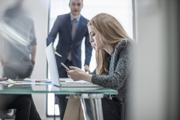 Businesswoman using cell phone and laptop during a meeting in conference room - ZEF007974