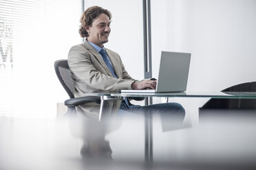 Smiling businessman at desk with laptop - ZEF007985