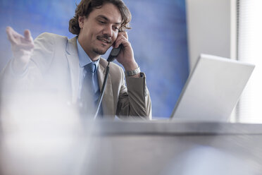 Businessman at desk with laptop on the phone - ZEF007990