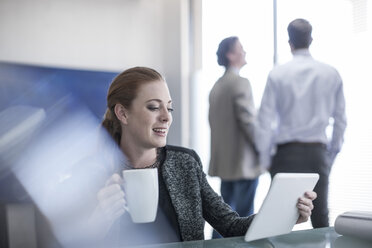 Lächelnde Frau im Büro, die eine Tasse Kaffee und ein digitales Tablet hält - ZEF007994