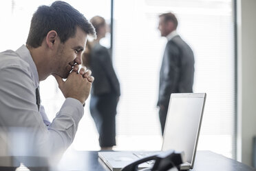 Smiling businessman in office looking at laptop - ZEF007998